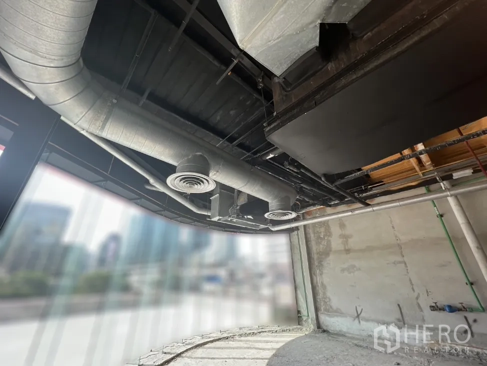 零售空间 出租在Pathum Wan, Bangkok - 弧形玻璃店面与金属风管，窗外可见城市景观。