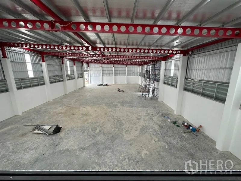 Warehouse for rent or sale in Lam Luk Ka, Pathum Thani - Mezzanine view across the clear warehouse floor and red truss roof structure.