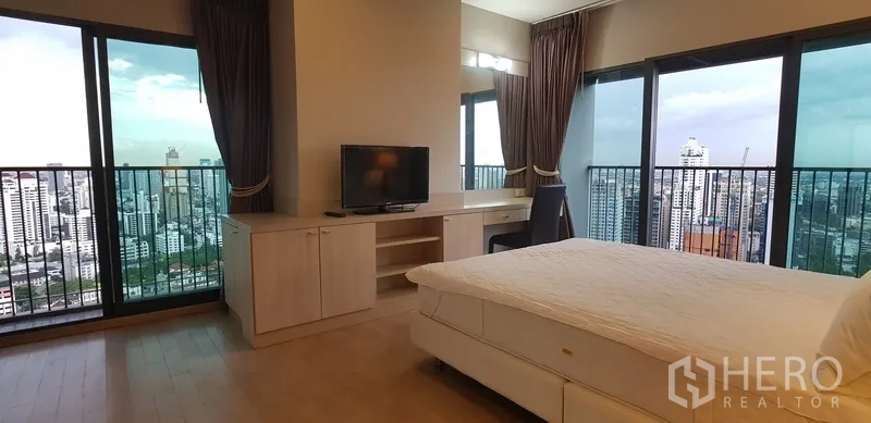 คอนโด ให้เช่าในKhlong Toei, Bangkok - ห้องนอนมุมอาคารพร้อมโต๊ะทำงาน ตู้ทีวี และระเบียงรอบมุมวิวเมือง