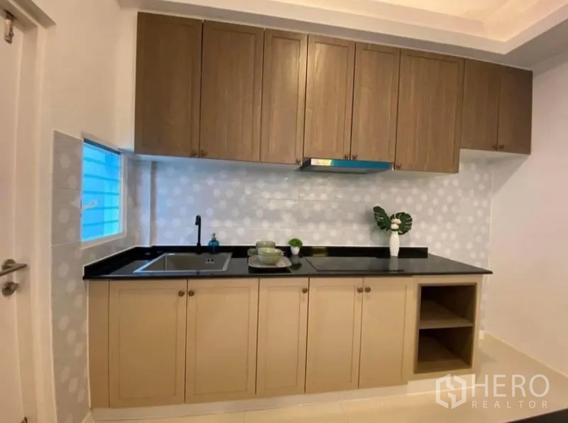 联排别墅 出租在Prawet, Bangkok - 一字型厨房，木质橱柜，黑色台面与圆点防溅墙。