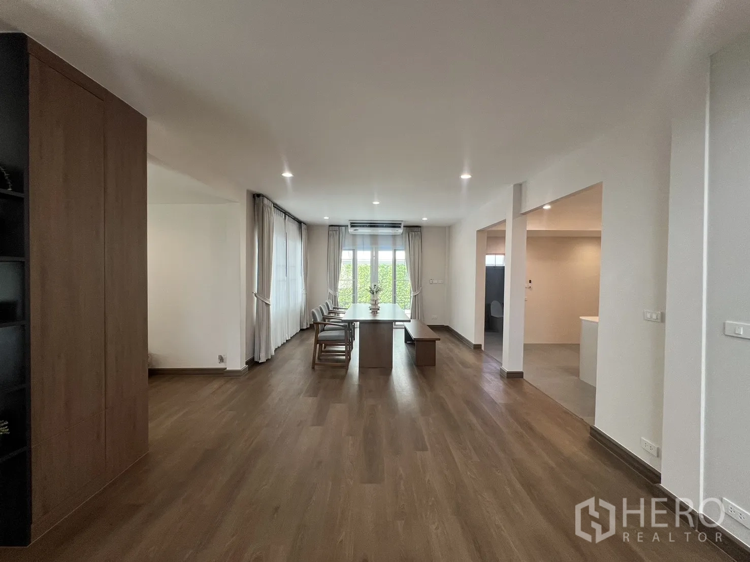 独立式住宅 出租在Mueang Samut Prakan, Samut Prakan - 餐厅内长木桌，大窗与窗帘采光充足。