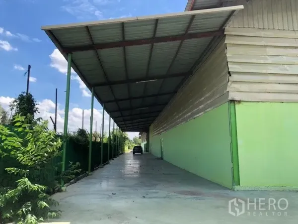 Factory for rent in Sam Khok, Pathum Thani - Long covered loading bay along the side of the factory with metal roof and concrete driveway.