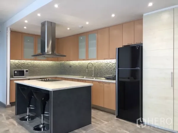 公寓 出租在Sathon, Bangkok - 现代U形厨房，带中岛、不锈钢烟机、浅木色橱柜与黑色冰箱。