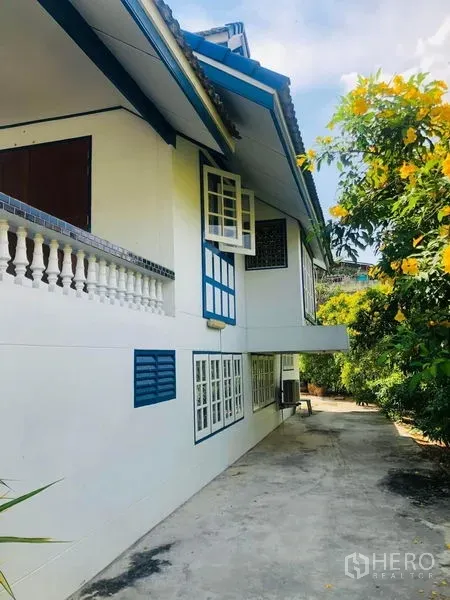 บ้าน ให้เช่าในKhlong San, Bangkok - มุมข้างบ้านพร้อมหน้าต่างเปิดและทางเดินสวนใต้ร่มไม้ดอก