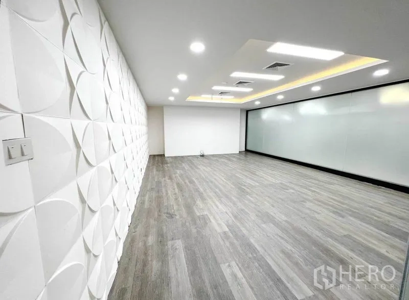 办公空间 出租在Phaya Thai, Bangkok - 明亮的开放式办公室，灰色木纹地面，白色3D造型墙，嵌入式灯光与整面磨砂玻璃墙。