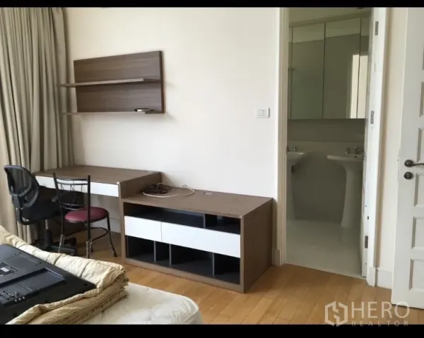 Condominium for rent in Khlong Toei, Bangkok - Workstation with desk, chair, wall shelves and TV console facing a bright bathroom.