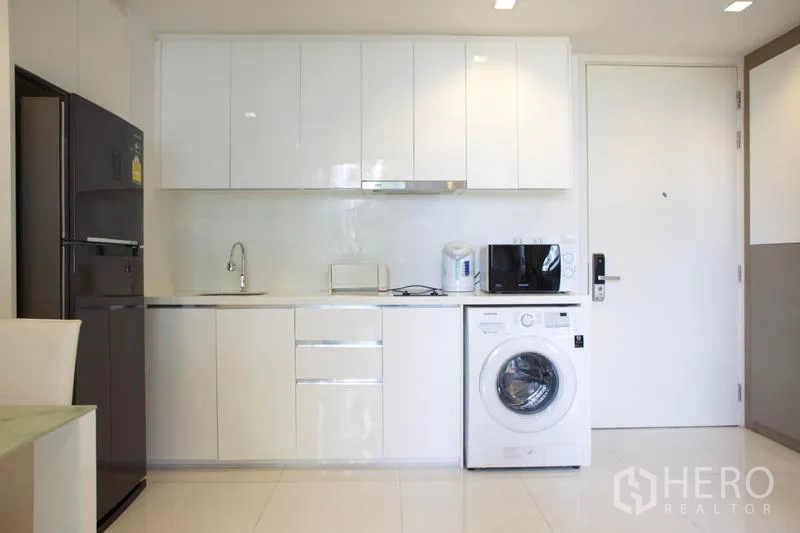 Condominium for rent in Sathon, Bangkok - Modern white kitchen with full cabinetry, refrigerator, sink and front‑load washing machine.