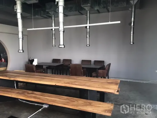 พื้นที่ขายปลีก ให้เช่าในWatthana, Bangkok - โซนรับประทานอาหารแบบเปิด โต๊ะและม้านั่งไม้ยาว พร้อมท่อดูดควันแขวนและผนังสีเทา