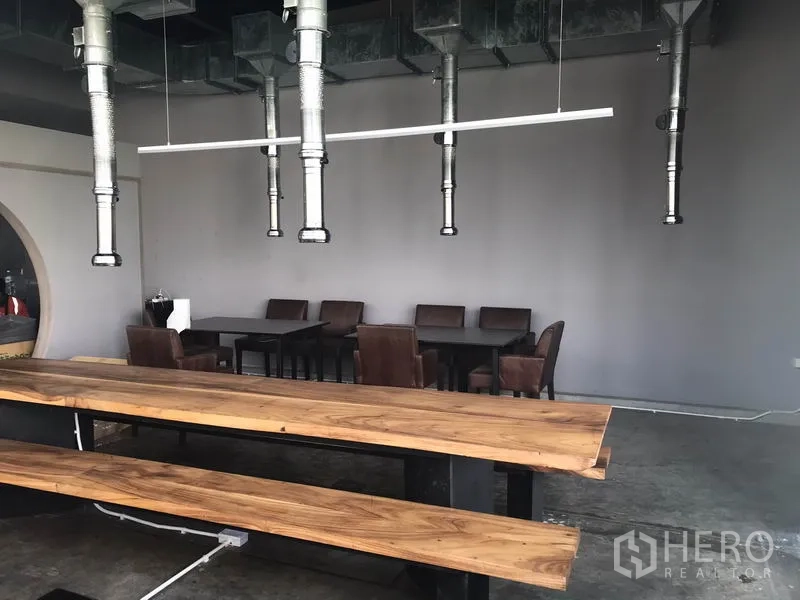 พื้นที่ขายปลีก ให้เช่าในWatthana, Bangkok - โซนรับประทานอาหารแบบเปิด โต๊ะและม้านั่งไม้ยาว พร้อมท่อดูดควันแขวนและผนังสีเทา