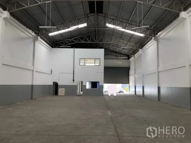 Factory for rent in Khlong Luang, Pathum Thani - Warehouse interior facing the loading roller door and mezzanine office block beneath an arched roof.