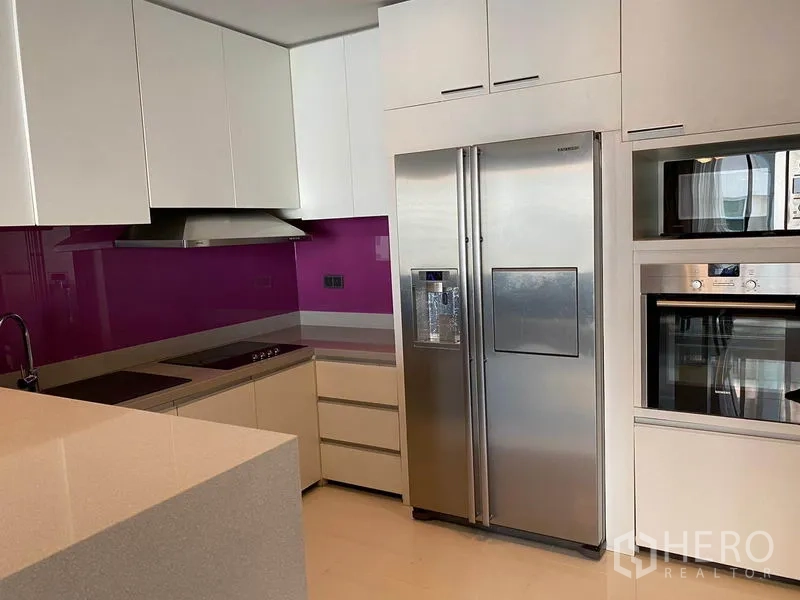 公寓 出租在Khlong Toei, Bangkok - 现代L形厨房，白色橱柜、亮紫色挡板、电磁炉与不锈钢对开门冰箱。
