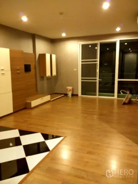 Condominium for rent in Phra Khanong, Bangkok - Spacious living room with media cabinetry, wood floors, and sliding glass doors opening to a balcony.