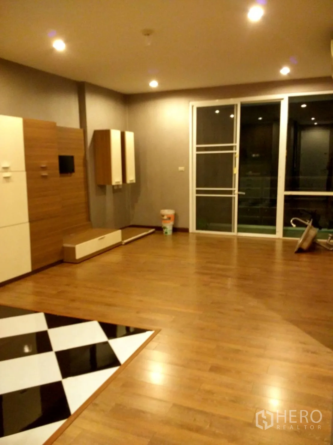 Condominium for rent in Phra Khanong, Bangkok - Spacious living room with media cabinetry, wood floors, and sliding glass doors opening to a balcony.