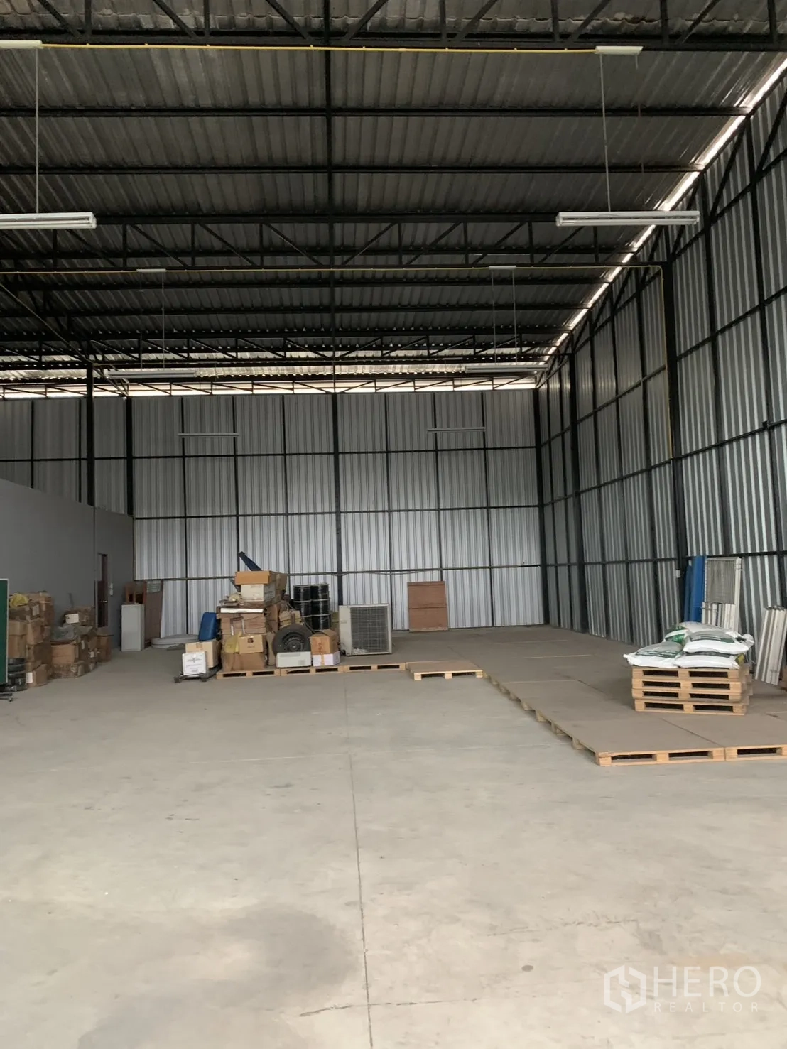 Warehouse for sale in Bang Len, Nakhon Pathom - Spacious warehouse interior with high steel truss roof, concrete floor, pallets and boxes.