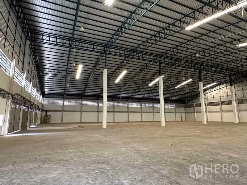 Warehouse for rent in Samut Prakan - Spacious warehouse interior with high steel truss roof, white columns and bright strip lighting.