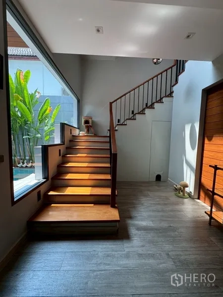 Semi-detached House for rent in Watthana, Bangkok - Staircase beside a large window overlooking poolside greenery.