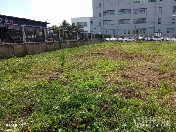 Land for rent in Khan Na Yao, Bangkok - Close view of leveled land next to a black commercial building and boundary wall.