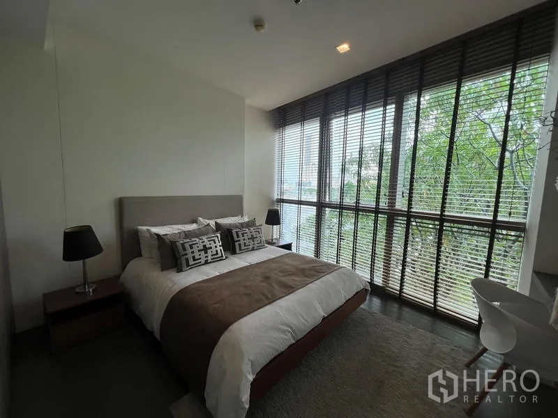 คอนโด ขายในKhlong San, Bangkok - ห้องนอนสว่าง เตียงควีน โคมข้างเตียง และวิวต้นไม้ผ่านหน้าต่างบานใหญ่