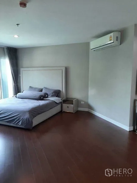 Condominium for rent or sale in Huai Khwang, Bangkok - Spacious master bedroom with king bed, wood floors, air conditioner and balcony access.