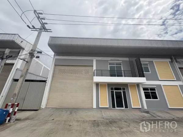 工厂 出租在Phra Samut Chedi, Samut Prakan - 现代两层厂房外立面，设宽大卷帘门、阳台和前方硬铺装卸区。