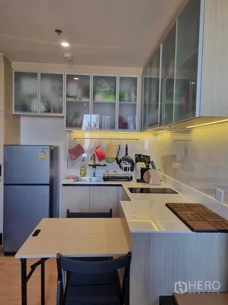 คอนโด ให้เช่าในWatthana, Bangkok - ครัวสมัยใหม่ขนาดกะทัดรัด ตู้ไม้สีอ่อน บานตู้กระจก เตา ทำอาหาร ตู้เย็น และโต๊ะทานข้าวเล็ก