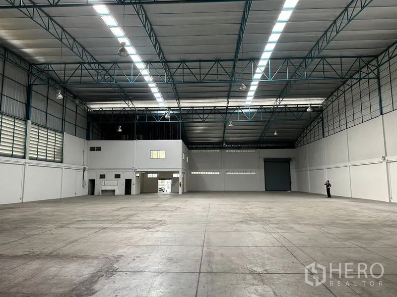 工厂 出租在Si Racha, Chon Buri - 仓库内部朝向装卸卷闸门，旁侧为办公室区，宽阔混凝土地坪。