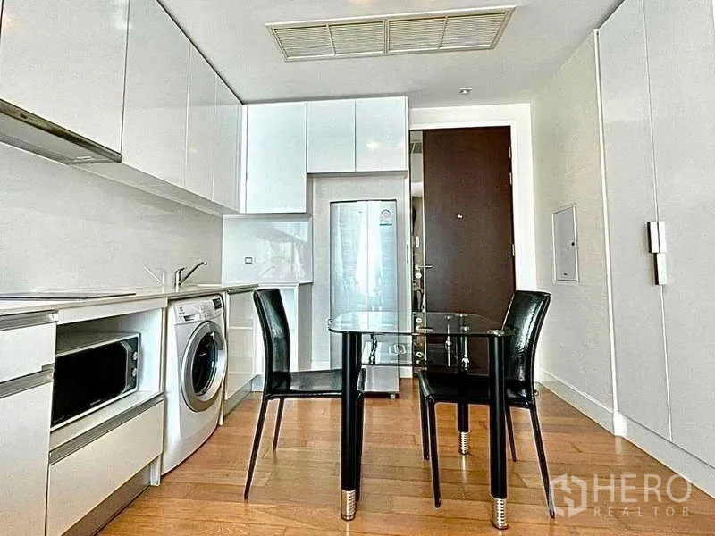 Condominium for rent in Bangkok - Compact kitchen with glossy cabinets, washer, microwave and glass dining table.