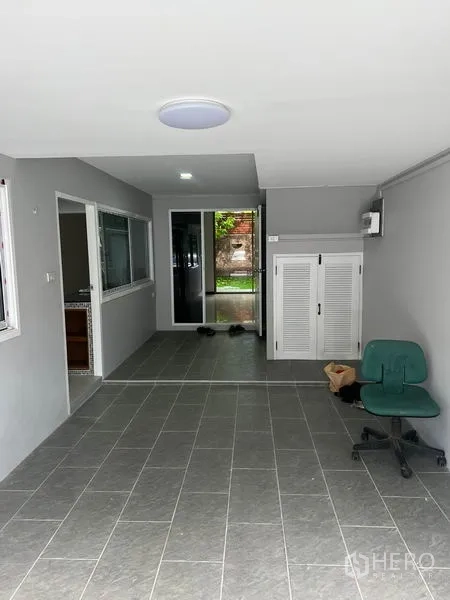 Townhouse for rent in Watthana, Bangkok - Ground-floor multipurpose area with gray floor tiles and sliding glass door to the garden.