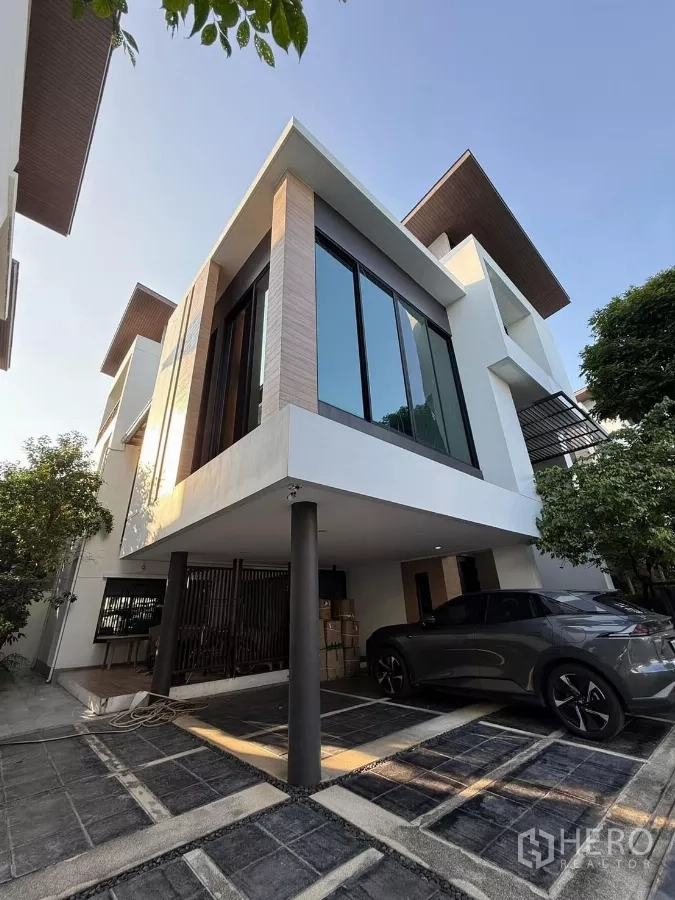 Detached House for rent or sale in Bueng Kum, Bangkok - Corner exterior view of the detached house showing floor-to-ceiling windows, raised carport and tiled driveway.