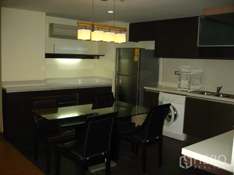 คอนโด ให้เช่าในWatthana, Bangkok - ครัวเปิดพร้อมตู้สีเข้ม ตู้เย็น เครื่องซักผ้า และโต๊ะอาหารกระจกใต้โคมไฟแขวน