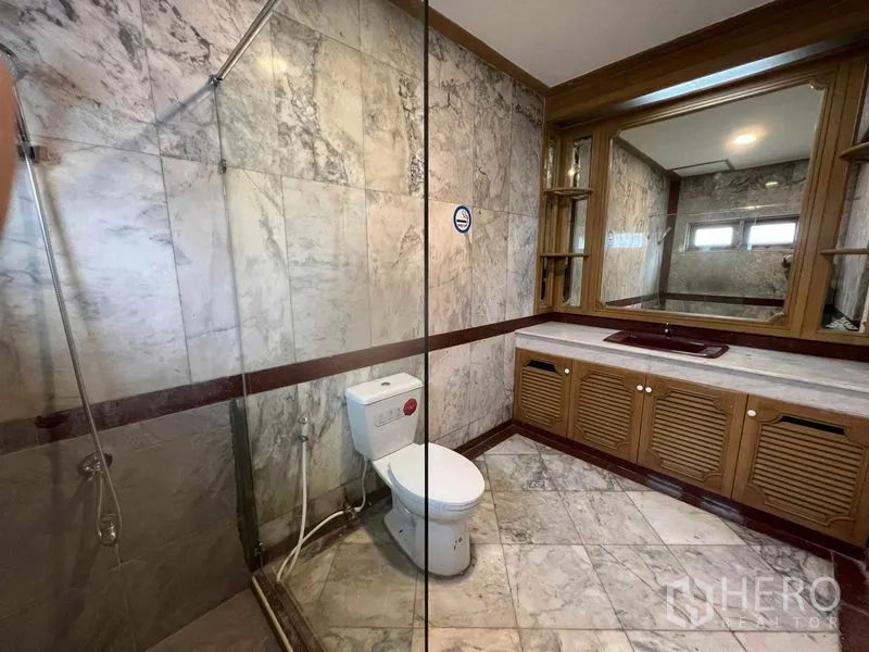 Detached House for sale in Bang Na, Bangkok - Marble-clad bathroom with glass shower, large mirror and wooden vanity.