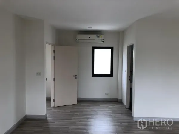 Townhouse for rent or sale in Saphan Sung, Bangkok - Upper-floor bedroom with wood-look flooring, window, air conditioner and ensuite door.