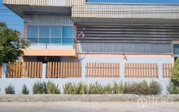 Warehouse for sale in Pathum Thani - Front elevation showing office windows and balcony above a secure fence line.