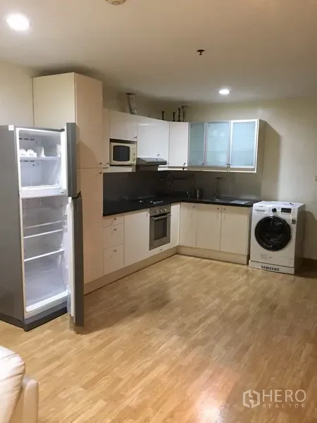 Condominium for rent in Pathum Wan, Bangkok - L-shaped kitchen with white cabinetry, oven, microwave, refrigerator and washing machine.