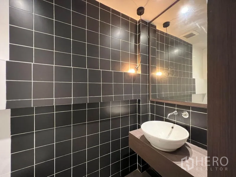 店屋 出租 - 现代化洗手间，黑色瓷砖墙与台上盆。