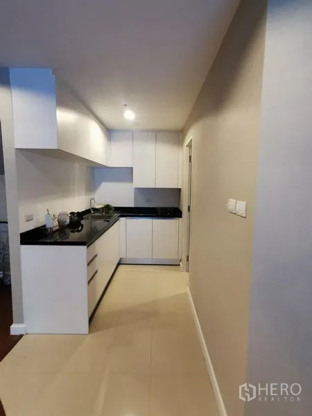 Condominium for rent or sale in Huai Khwang, Bangkok - Galley kitchen with white cabinetry and black stone countertop.
