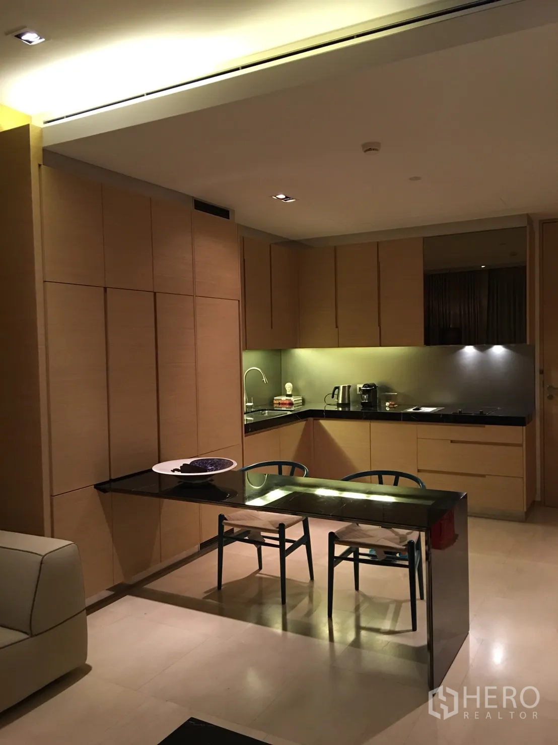 公寓 出租或出售在Bang Rak, Bangkok - 开放式厨房，浅木柜体、黑色石材台面与双人餐桌相连。