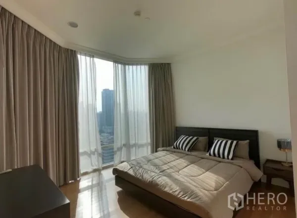 Condominium for rent in Watthana, Bangkok - Corner bedroom with king bed, striped cushions and panoramic windows facing the skyline.