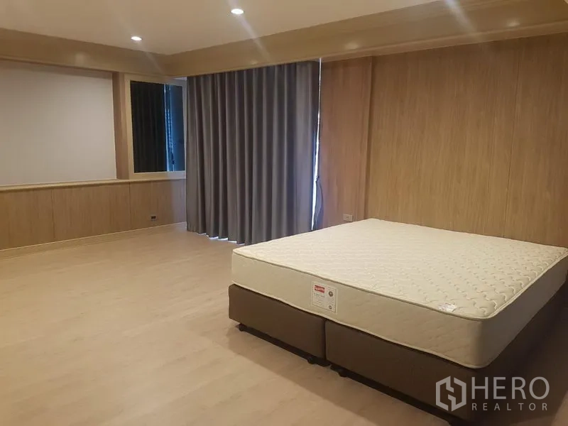 Apartment for rent in Khlong Toei, Bangkok - Spacious master bedroom with king bed, wood panel walls and blackout curtains