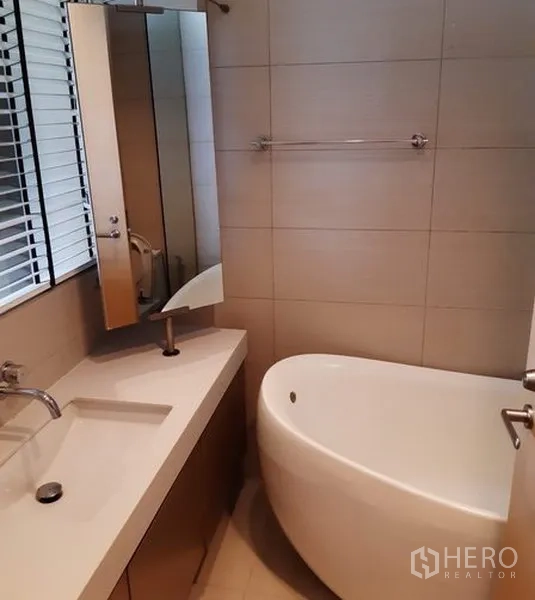 公寓 出租在Khlong Toei, Bangkok - 卫浴间铺瓷砖，设长台盆、镜柜与椭圆形浸泡浴缸。