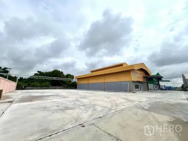 Warehouse for rent in Lat Lum Kaeo, Pathum Thani - Wide concrete yard and modern yellow steel-clad warehouse exterior under cloudy sky.