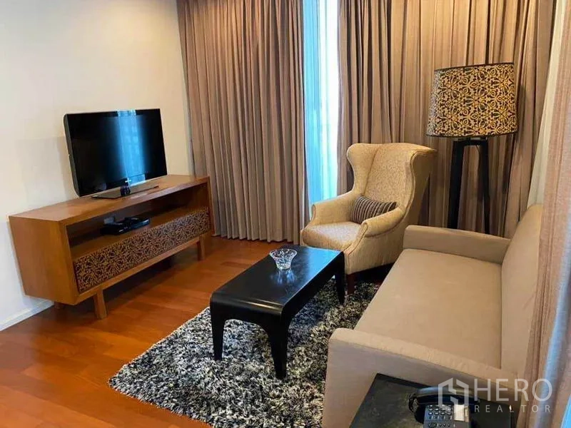 Condominium for rent in Watthana, Bangkok - Living room with sofa, armchair, TV console, patterned floor lamp, and large curtains.