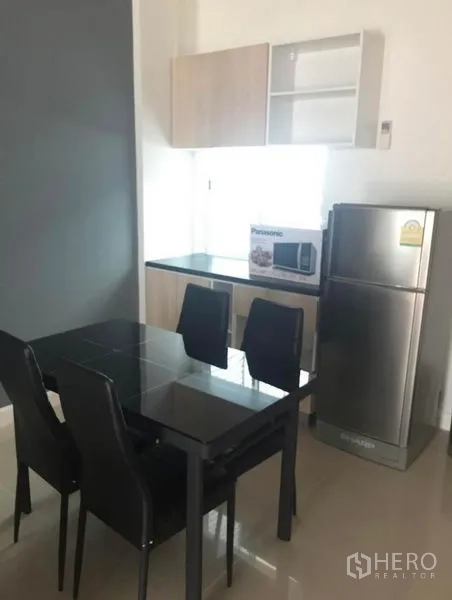 联排别墅 出租在Prawet, Bangkok - 小型厨房与餐区，黑色玻璃餐桌四椅，吊柜和不锈钢冰箱。