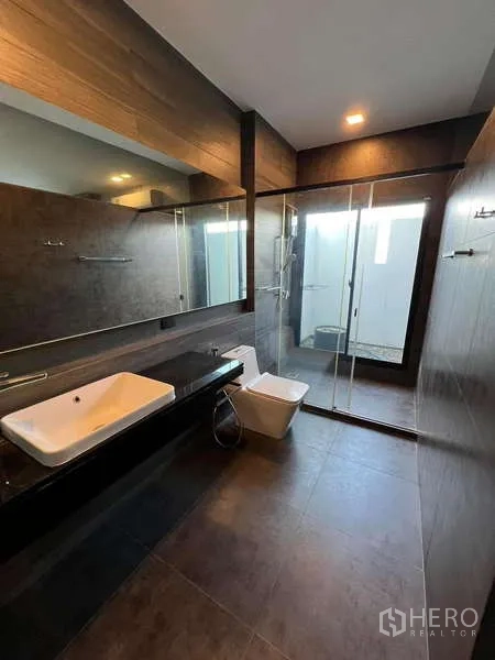 Detached House for rent or sale in Bang Phli, Samut Prakan - Contemporary bathroom with long vanity, glass shower enclosure and dark tiles.