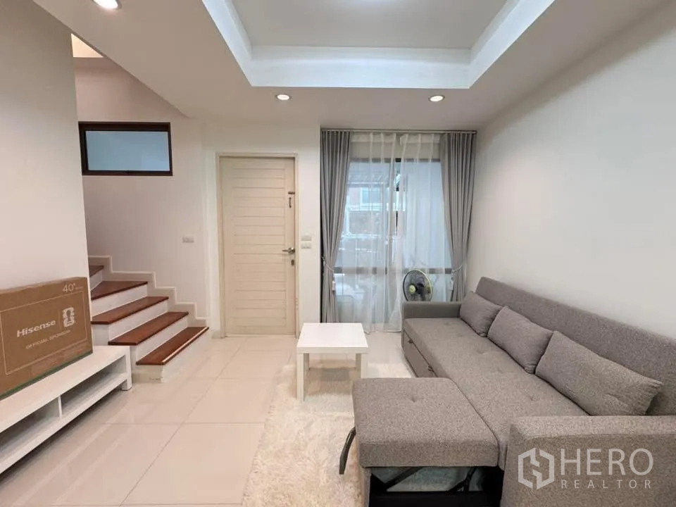 联排别墅 for rent in Phra Khanong, Bangkok - 客厅内有转角沙发、楼梯与大窗户。
