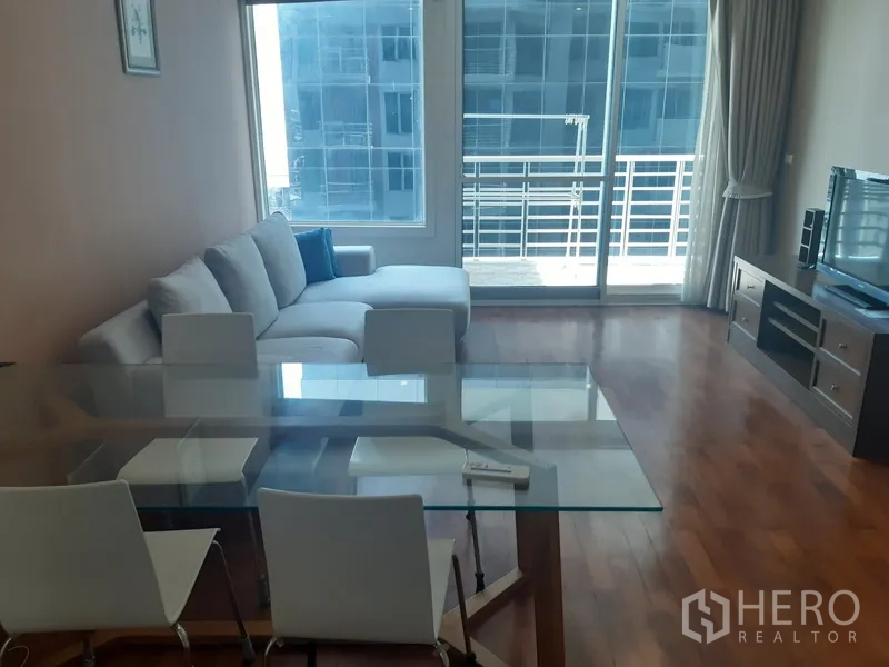 คอนโด ให้เช่าในKhlong Toei, Bangkok - ห้องนั่งเล่นพร้อมโซฟา L โต๊ะทานอาหารกระจก ชั้นวางทีวี และประตูกระจกบานเลื่อนสู่ระเบียงวิวเมือง