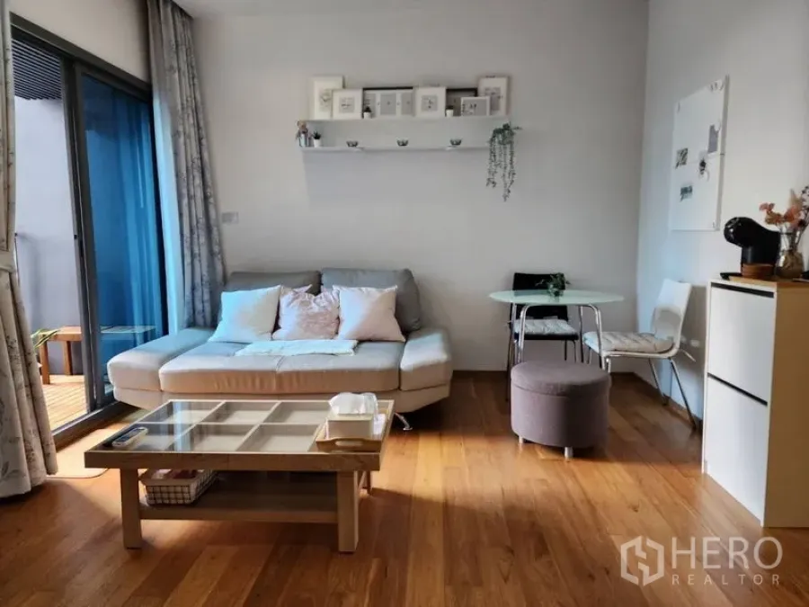 公寓 出租在Watthana, Bangkok - 明亮客厅，沙发与玻璃茶几，推拉门通向阳台，靠近BTS娜娜站的一卧公寓。