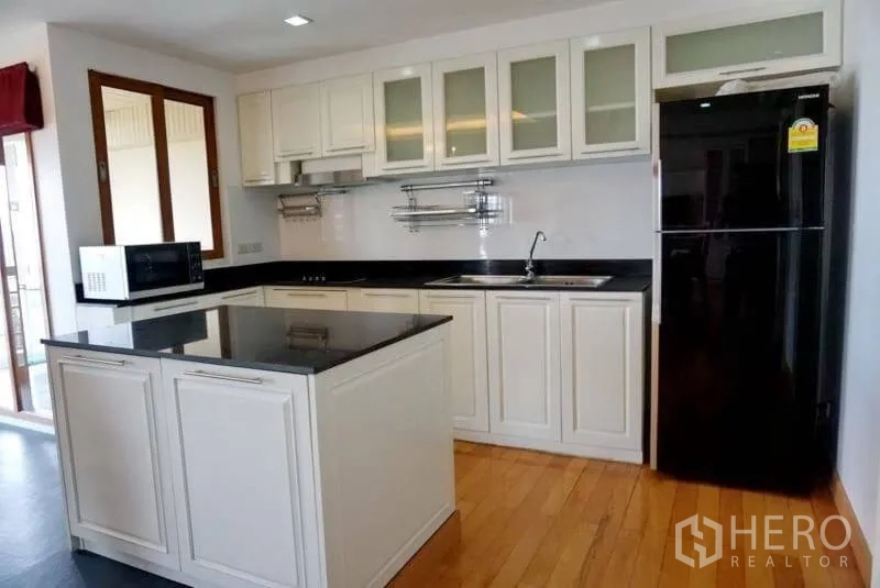 Condominium for rent in Watthana, Bangkok - Modern white kitchen with black stone countertops, island and full-size refrigerator.