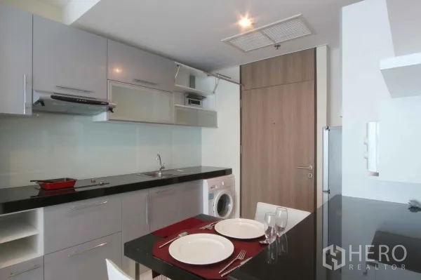 Condominium for rent in Khlong Toei, Bangkok - Modern kitchenette with glossy cabinets, black stone countertop, cooktop, range hood, and in‑unit washer in a Sukhumvit condo.