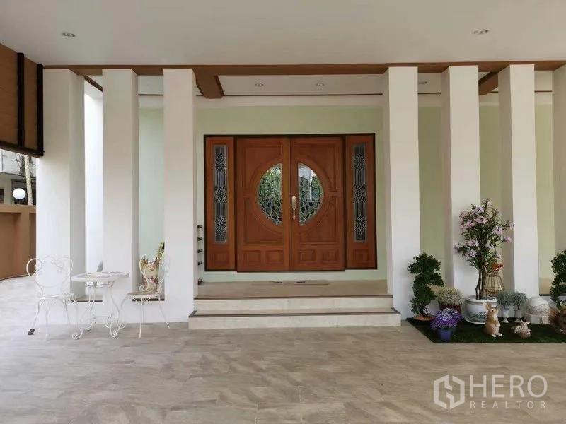 Detached House for rent in Prawet, Bangkok - Covered front porch featuring grand double wooden doors, columns, bistro set and potted plants.